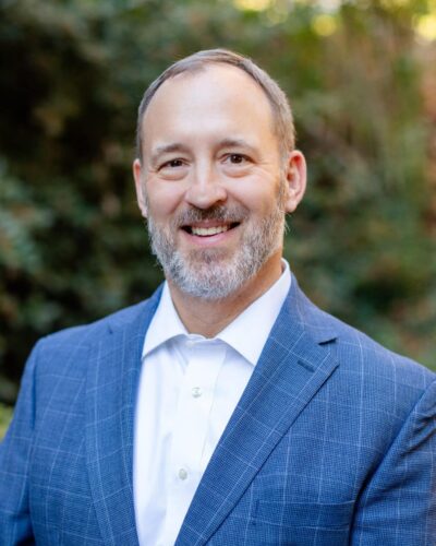 A Man Wearing A Suit And Tie Smiling At The Camera